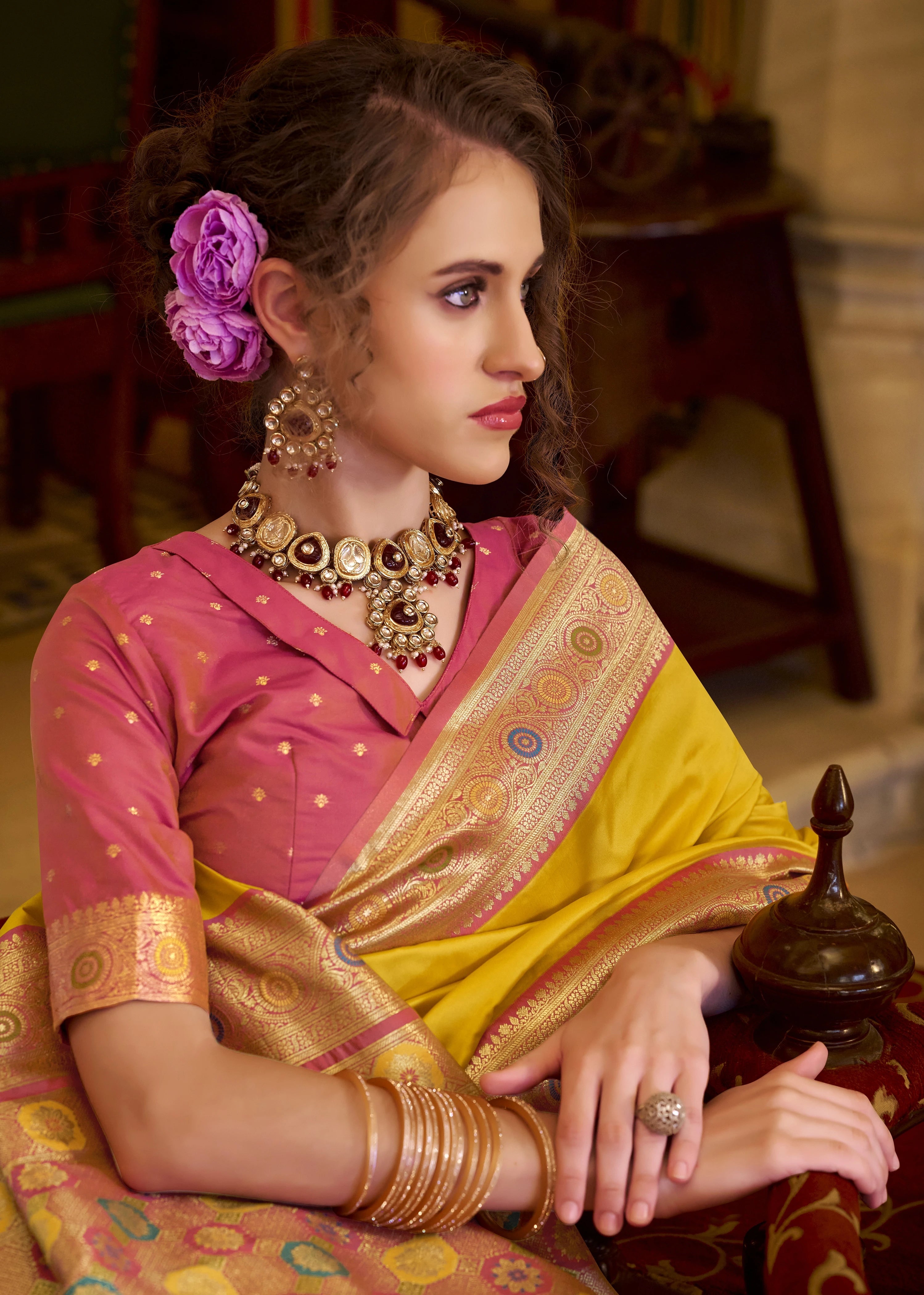 Woman in a traditional saree with jewelry and a purple flower in her hair.